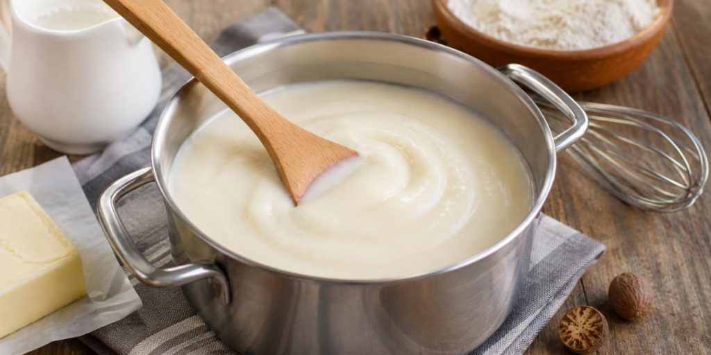 Salsa bechamel casera cremosa en cazo con cuchara de madera