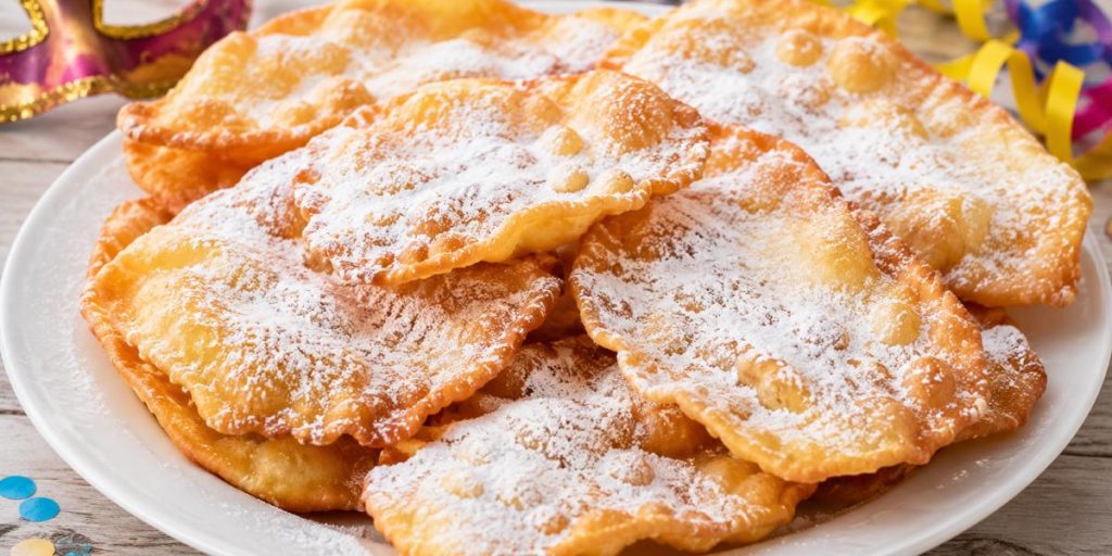 Orejas de Carnaval caseras espolvoreadas con azúcar glas sobre plato blanco