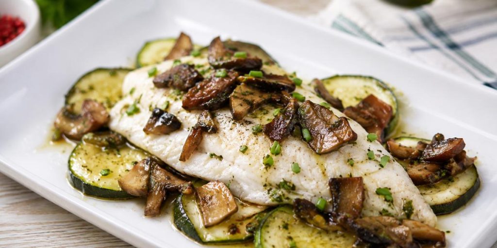 Filetes de dorada al horno con calabacín y boletus sobre plato blanco