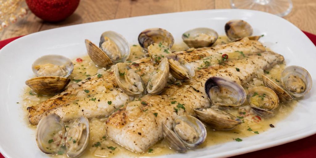 Lubina con almejas en salsa de vino blanco servida en plato blanco