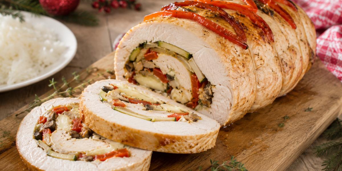 Pechuga de pavo rellena de vegetales y queso cortada en rodajas sobre tabla de madera