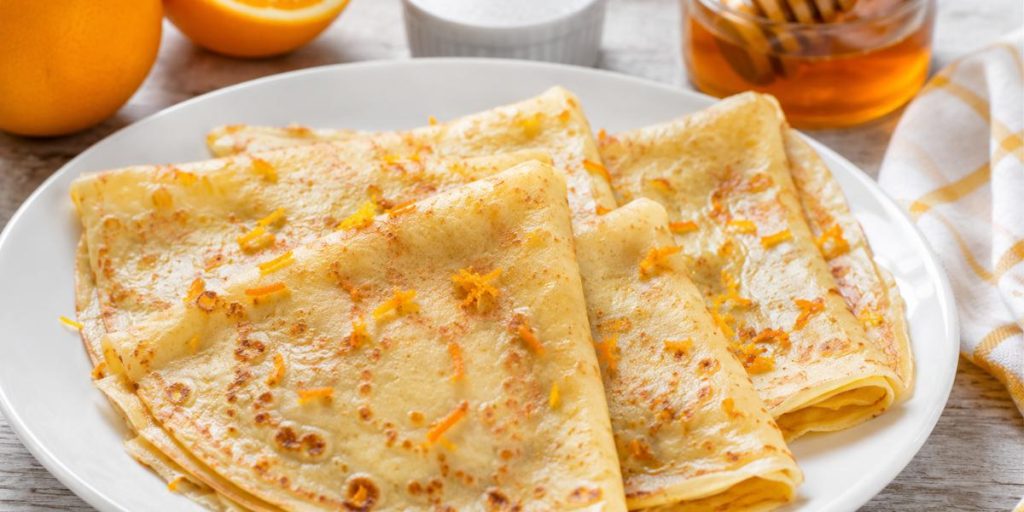 Filloas de leche caseras dobladas en plato blanco con ralladura de naranja